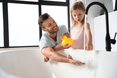 Photo of Father with his cute little daughter filling tub in bathroom