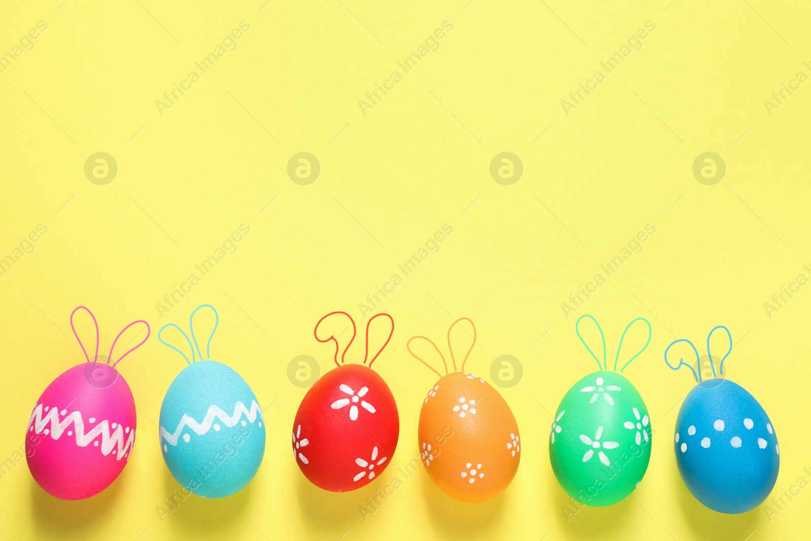 Image of Bright Easter eggs with cute bunny ears and space for text on yellow background, flat lay