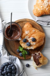 Delicious croissants with almond flakes, chocolate and blueberries served on white wooden table, flat lay