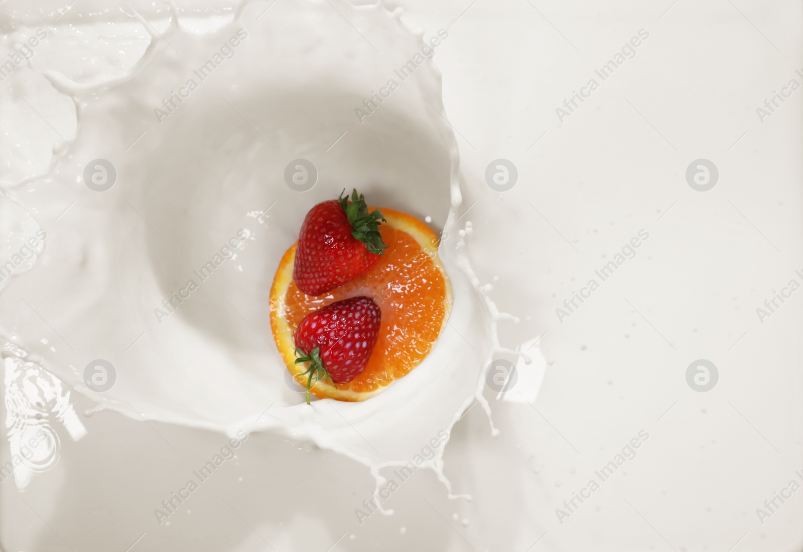 Photo of Slice of orange and strawberries falling in milk with splashes, top view