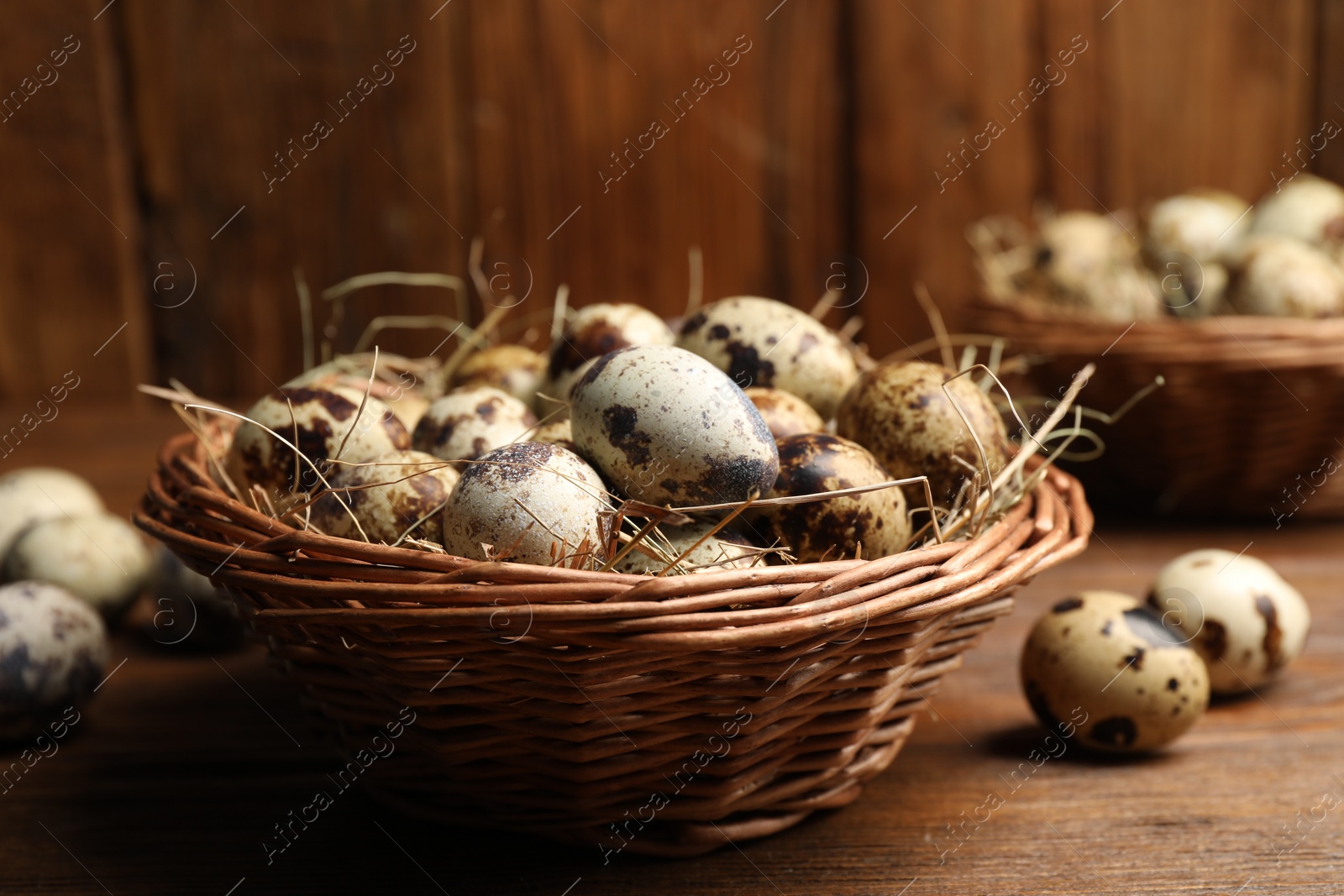 Photo of Wicker bowl with quail eggs and straw on wooden table, closeup