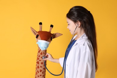 Photo of Little girl playing doctor with toy giraffe on yellow background. Pediatrician practice