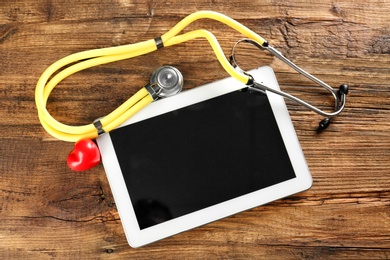Photo of Stethoscope, tablet and red heart on wooden background. Heart attack concept