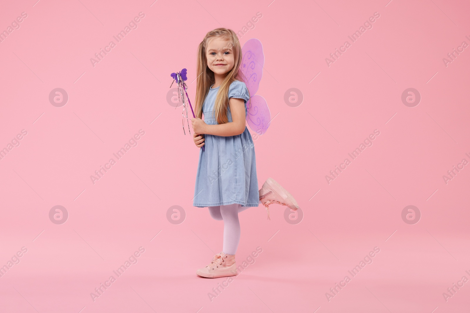 Photo of Cute little girl in fairy costume with violet wings and magic wand on pink background