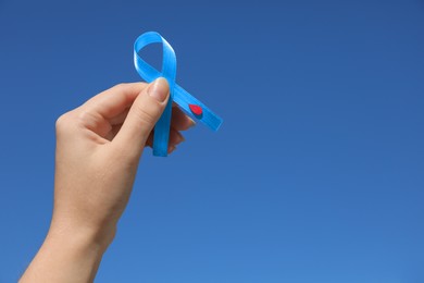 Photo of Woman holding light blue ribbon with paper blood drop against sky, closeup. Diabetes awareness