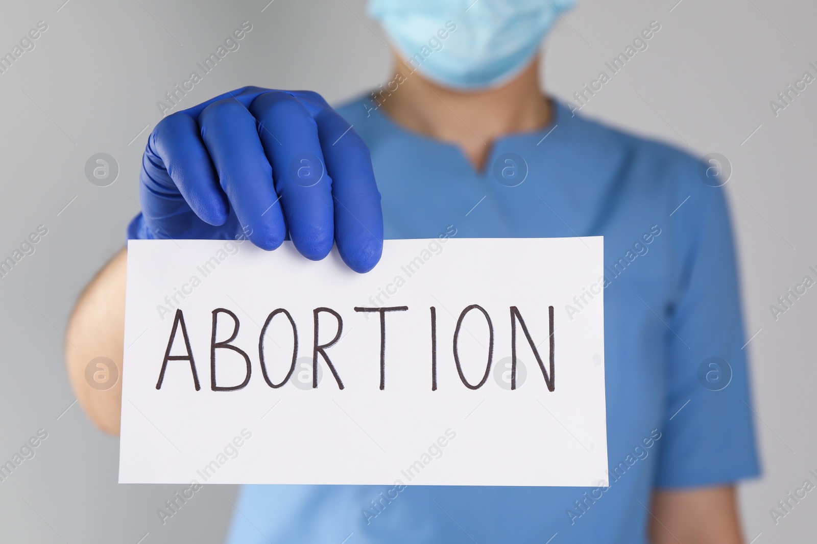 Photo of Doctor holding paper card with word ABORTION on light grey background, closeup