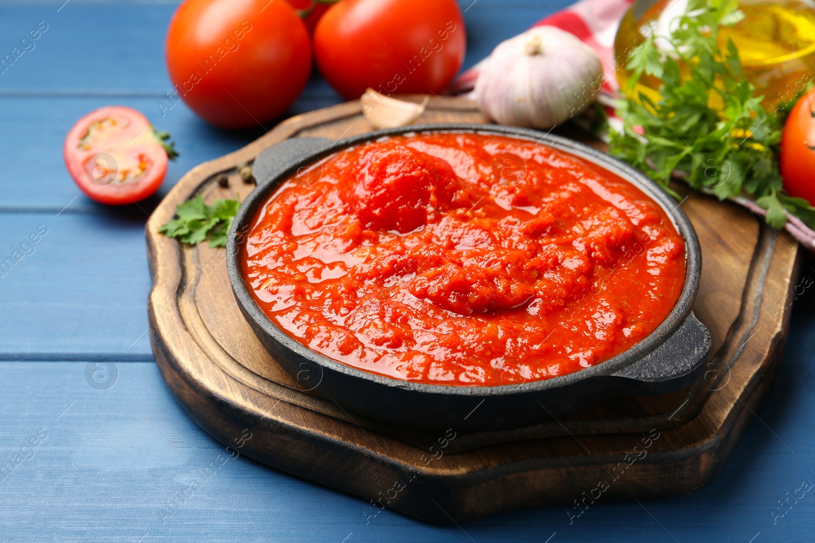 Photo of Homemade tomato sauce in bowl and ingredients on blue wooden table