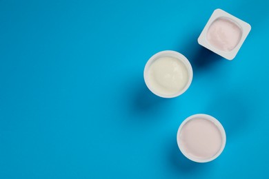 Photo of Plastic cups with tasty yogurt on light blue background, flat lay. Space for text