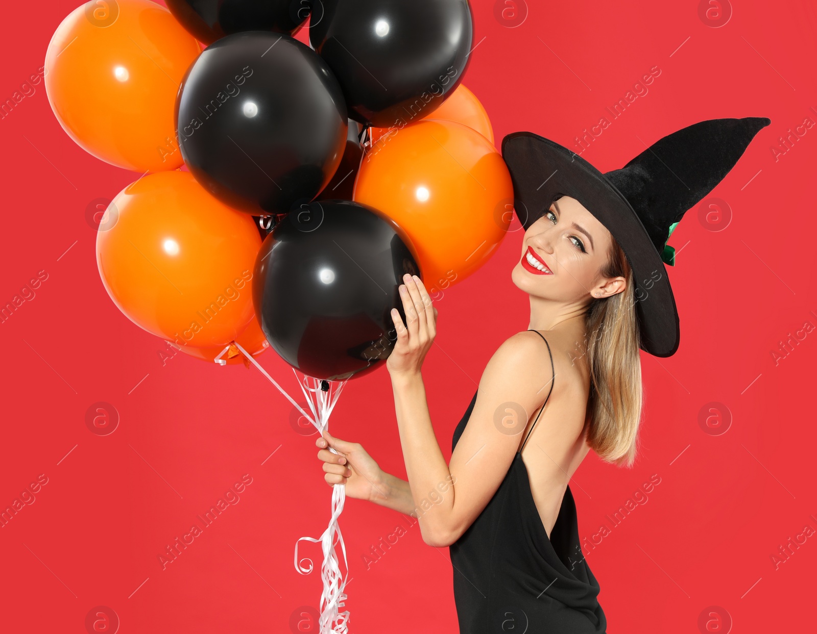 Photo of Beautiful woman wearing witch costume with balloons for Halloween party on red background