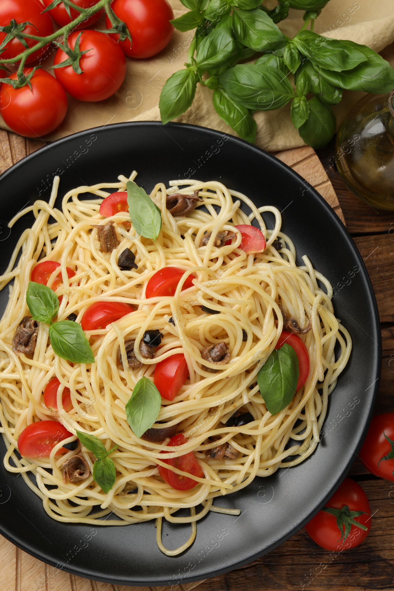 Photo of Delicious pasta with anchovies, tomatoes and basil on table, flat lay