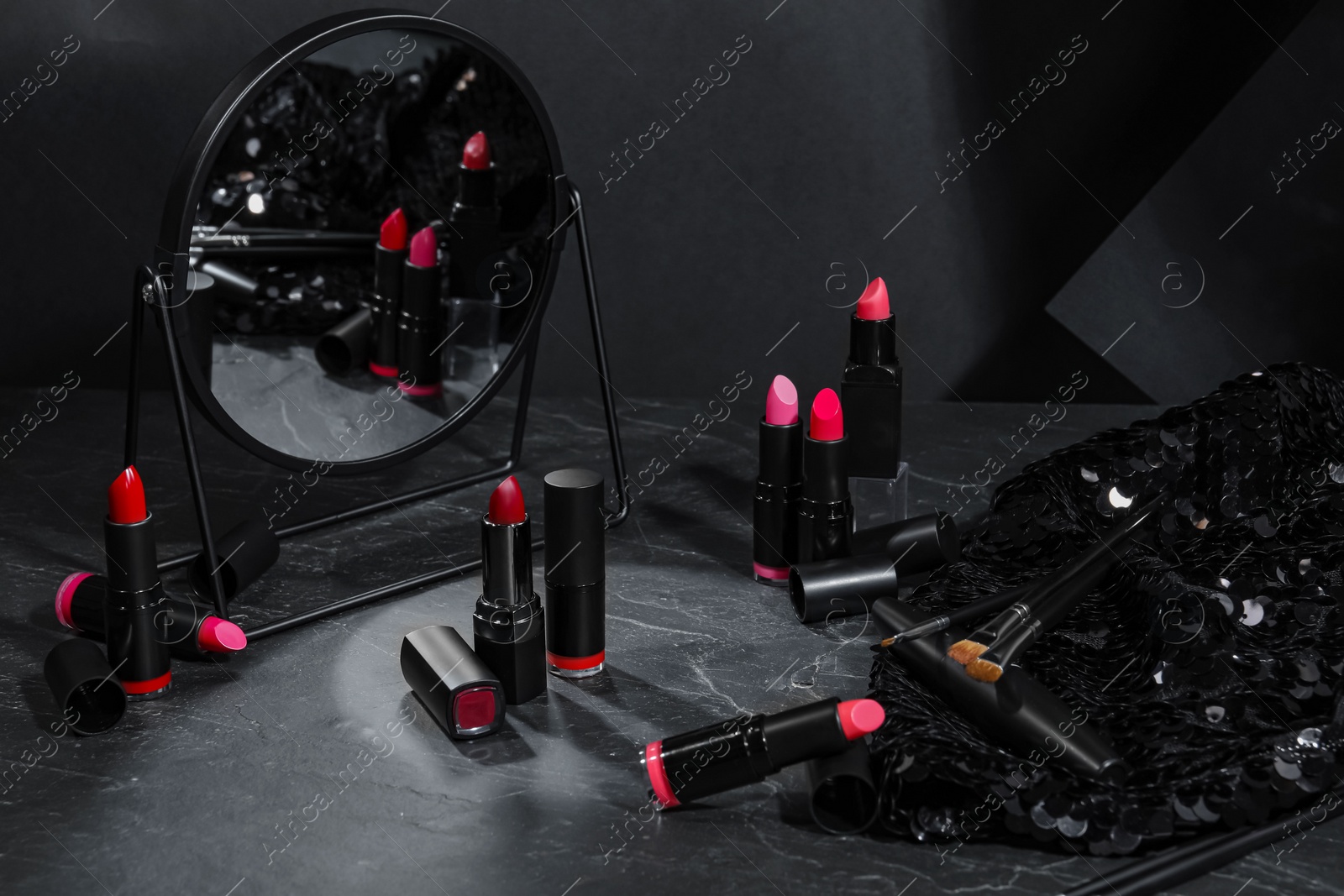 Photo of Beautiful lipsticks, mirror and different cosmetic products on grey marble table