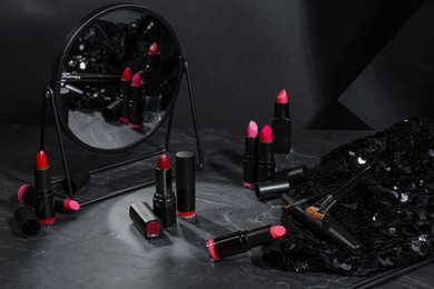 Beautiful lipsticks, mirror and different cosmetic products on grey marble table