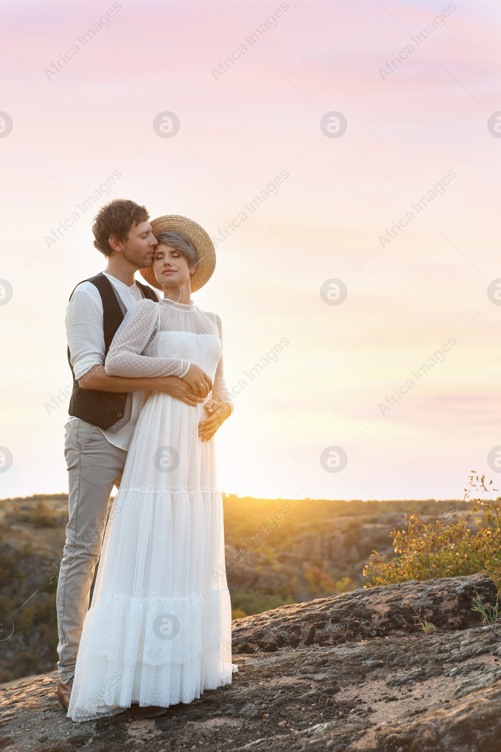 Photo of Happy newlyweds standing on rock at sunset