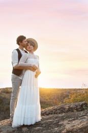 Photo of Happy newlyweds standing on rock at sunset