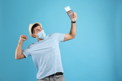 Photo of Emotional male tourist in protective mask holding passport with ticket on turquoise background, space for text