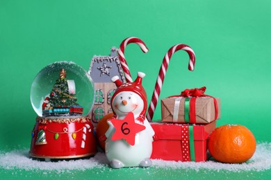 Photo of Decorative snowman with paper tag, gift boxes and festive decor on green background. December, 6 - Saint Nicholas Day