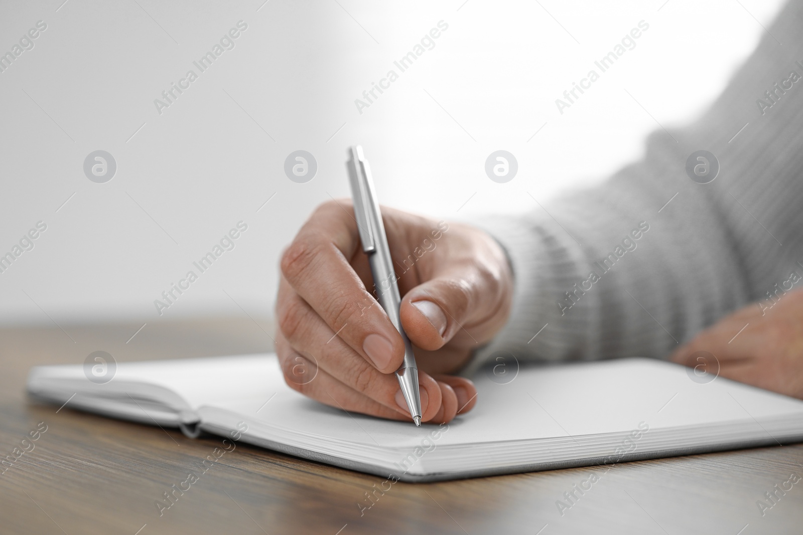 Photo of Man writing in notebook at wooden table indoors, closeup