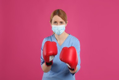 Photo of Doctor with protective mask and boxing gloves on pink background. Strong immunity concept