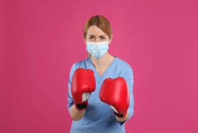 Doctor with protective mask and boxing gloves on pink background. Strong immunity concept