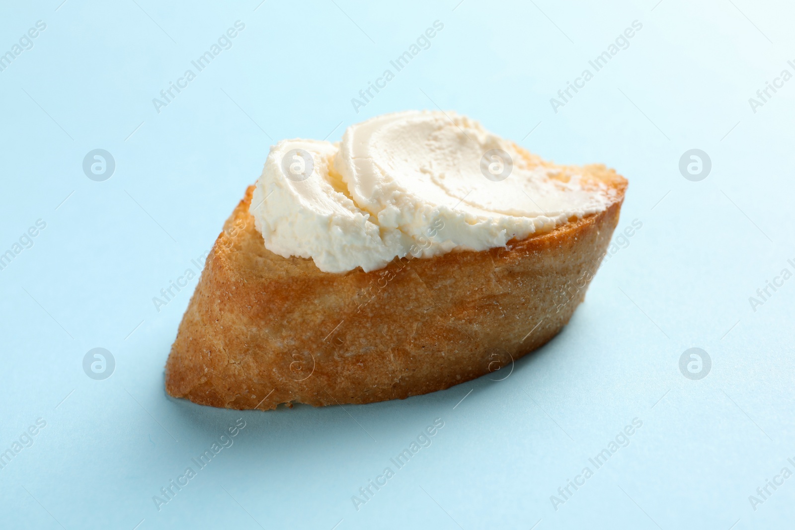 Photo of Piece of baguette with tasty cream cheese on color background