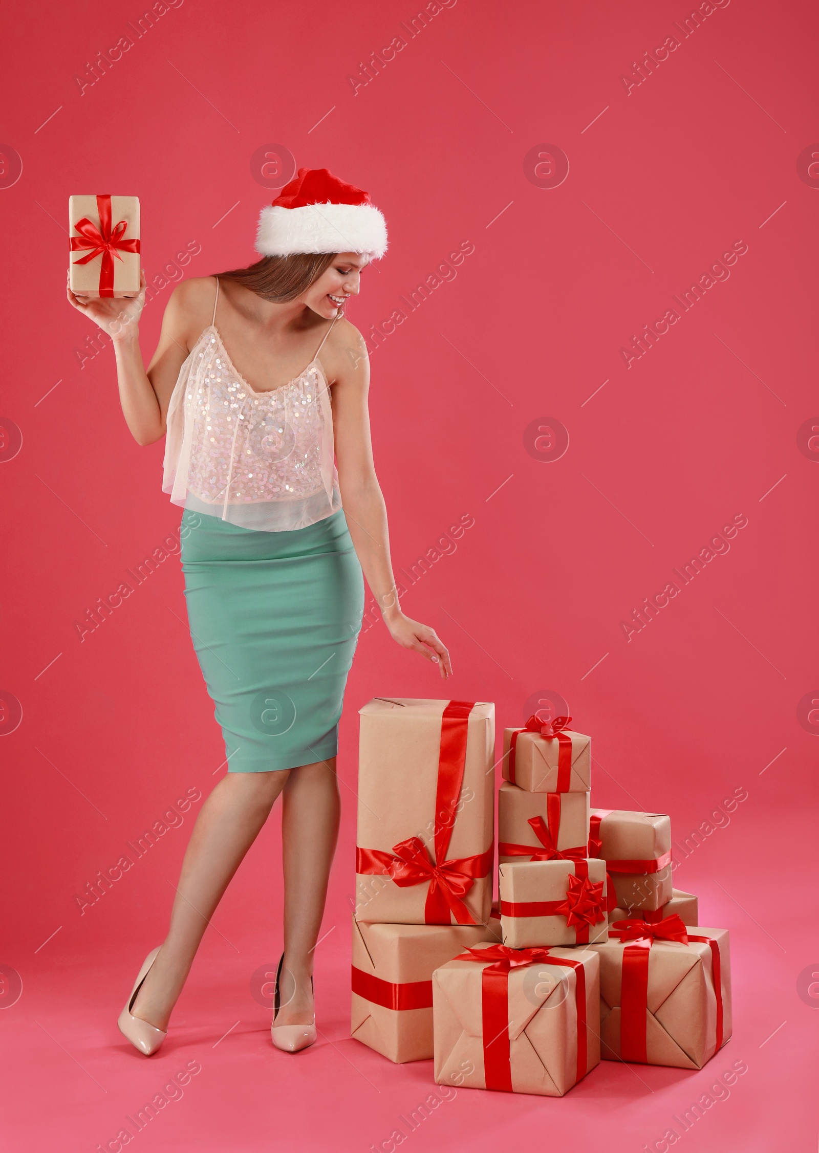 Photo of Happy young woman in Santa hat with Christmas gifts on pink background