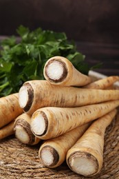 Photo of Raw parsley roots and fresh herb on wicker mat, closeup