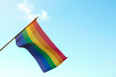 Bright LGBT flag against blue sky. Space for text