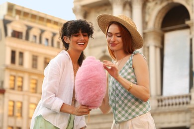 Happy friends with pink cotton candy on city street