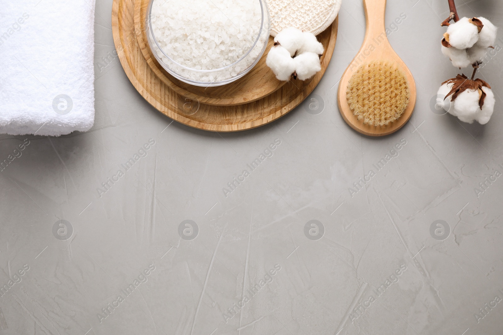 Photo of Sea salt and supplies for spa scrubbing procedure on grey stone background, flat lay