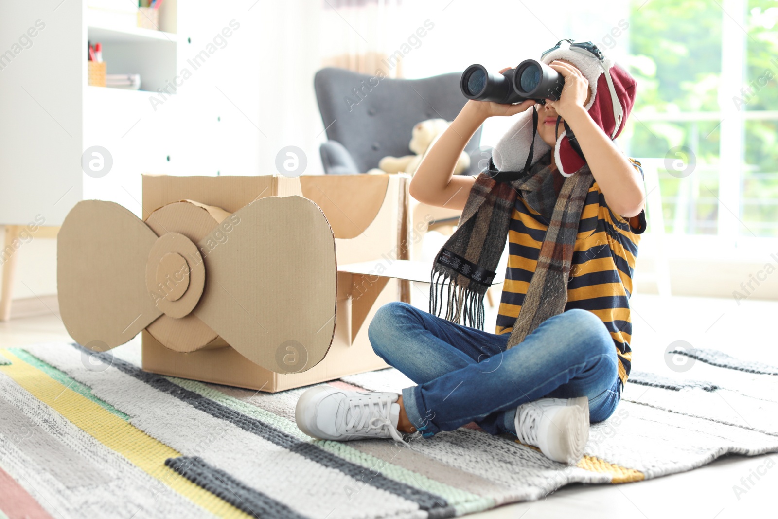 Photo of Adorable little child playing with binoculars and cardboard airplane indoors