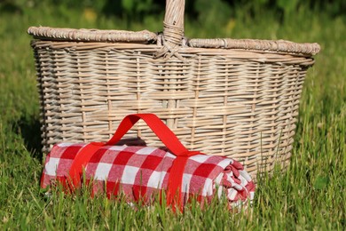 Rolled checkered tablecloth near picnic basket on green grass outdoors