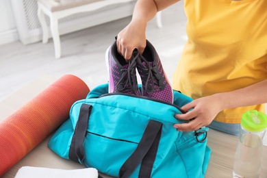 Photo of Young woman packing sports bag at home