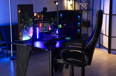 Photo of Playing video games. Stylish room interior with modern computer and gaming chair in neon lights