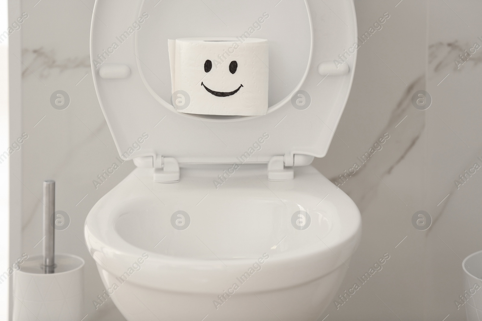 Photo of Roll of paper with funny face on toilet bowl in bathroom