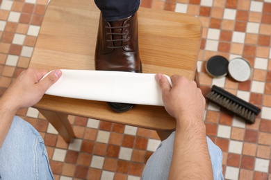 Photo of Man shining client's shoe on wooden stool indoors, closeup