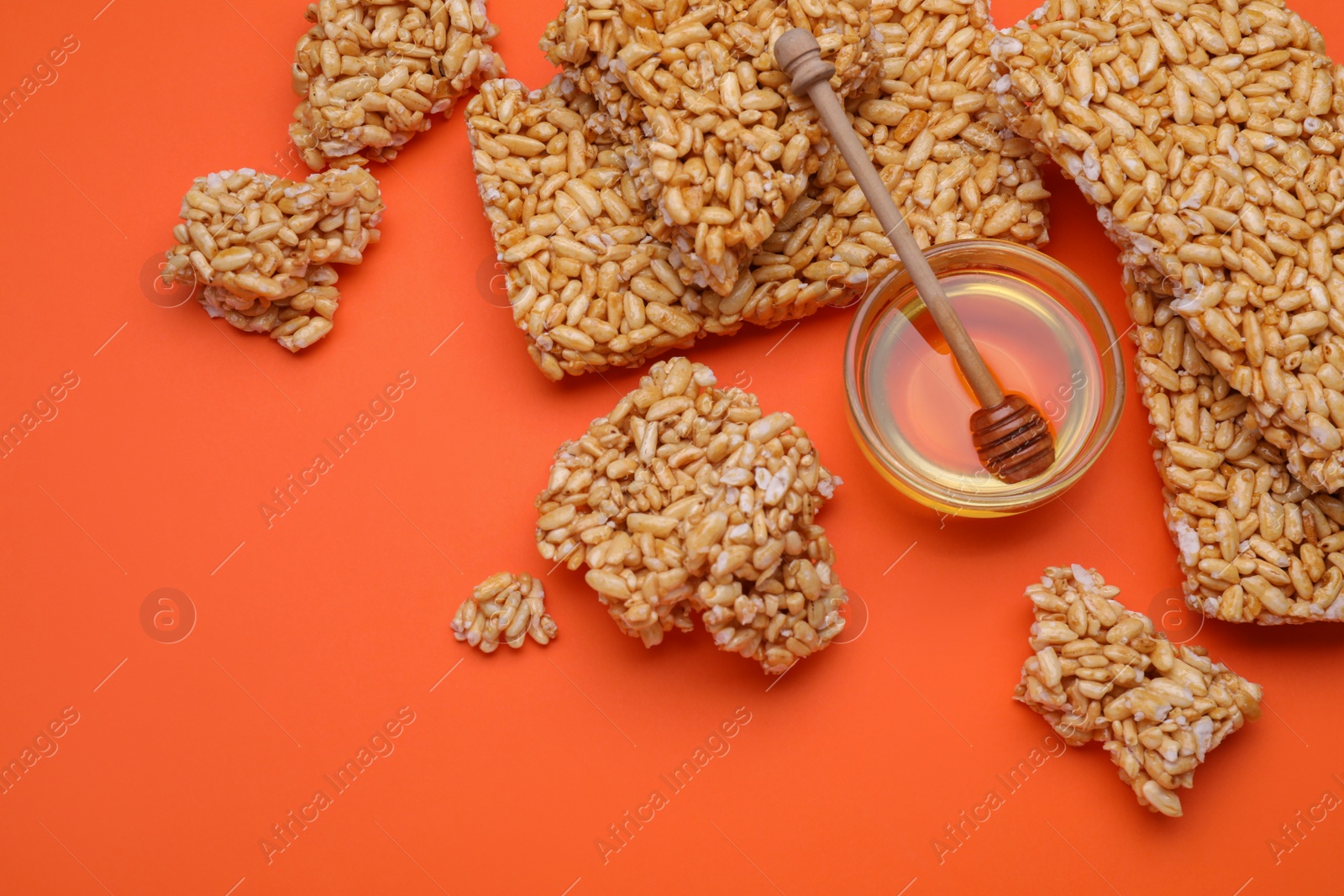 Photo of Puffed rice bars (kozinaki) and honey on orange background, flat lay. Space for text