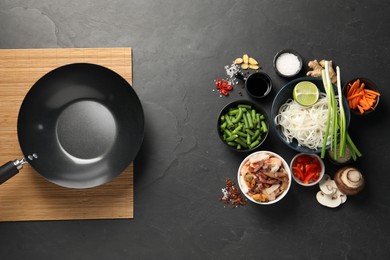 Flat lay composition with black wok, spices and products on dark textured table