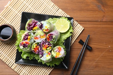 Photo of Delicious spring rolls, soy sauce and chopsticks on wooden table, top view