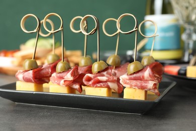 Tasty canapes with olives, prosciutto and cheese on grey table, closeup