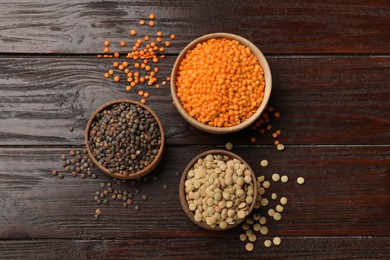 Different types of lentils in bowls on wooden table, flat lay