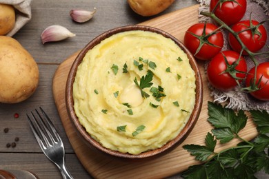 Photo of Bowl of freshly cooked mashed potatoes with parsley served on wooden table, flat lay