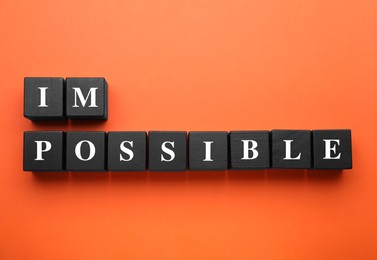 Photo of Motivation concept. Changing word from Impossible into Possible by removing black wooden cubes on orange background, flat lay