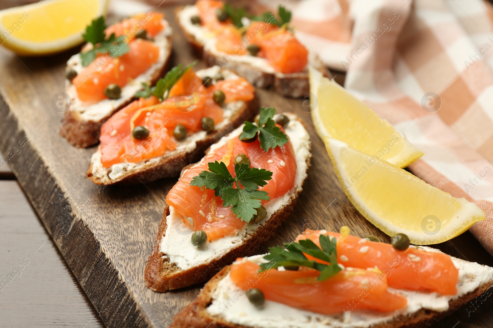 Photo of Tasty canapes with salmon, capers, lemon and cream cheese on wooden table, closeup