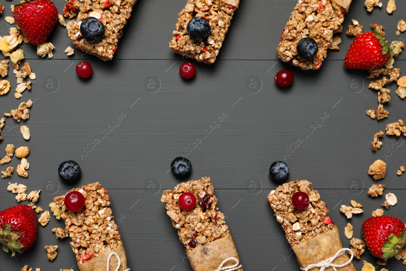 Photo of Tasty granola bars and ingredients on grey wooden table, flat lay. Space for text