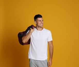 Handsome man with sports bag on yellow background