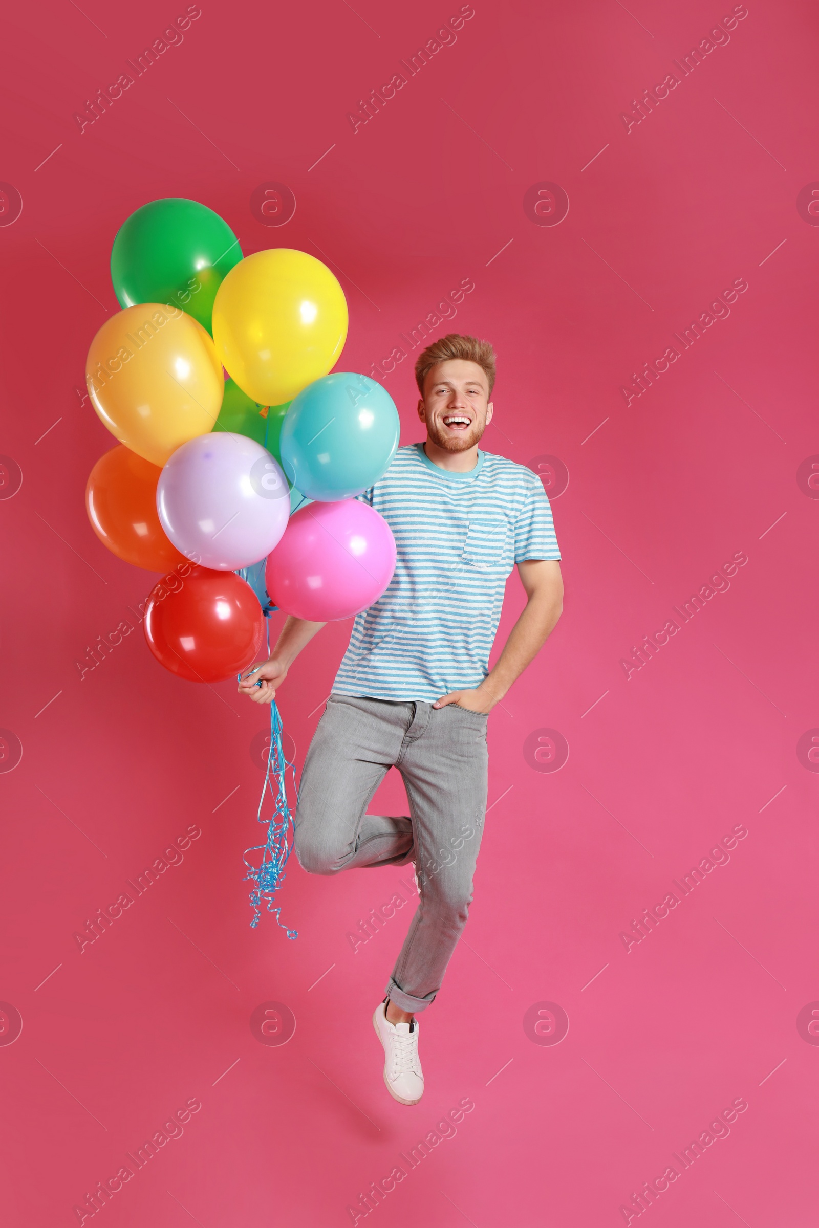 Photo of Young man jumping with bunch of colorful balloons on pink background