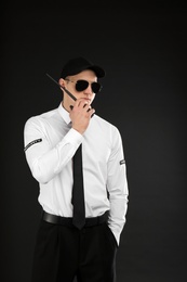 Male security guard using portable radio transmitter on dark background