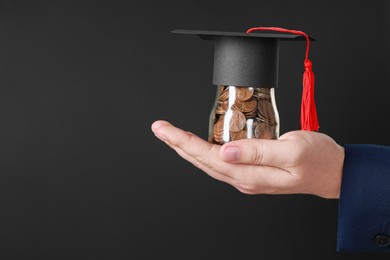 Photo of Man holding glass jar of coins and graduation cap against black background, closeup with space for text. Scholarship concept