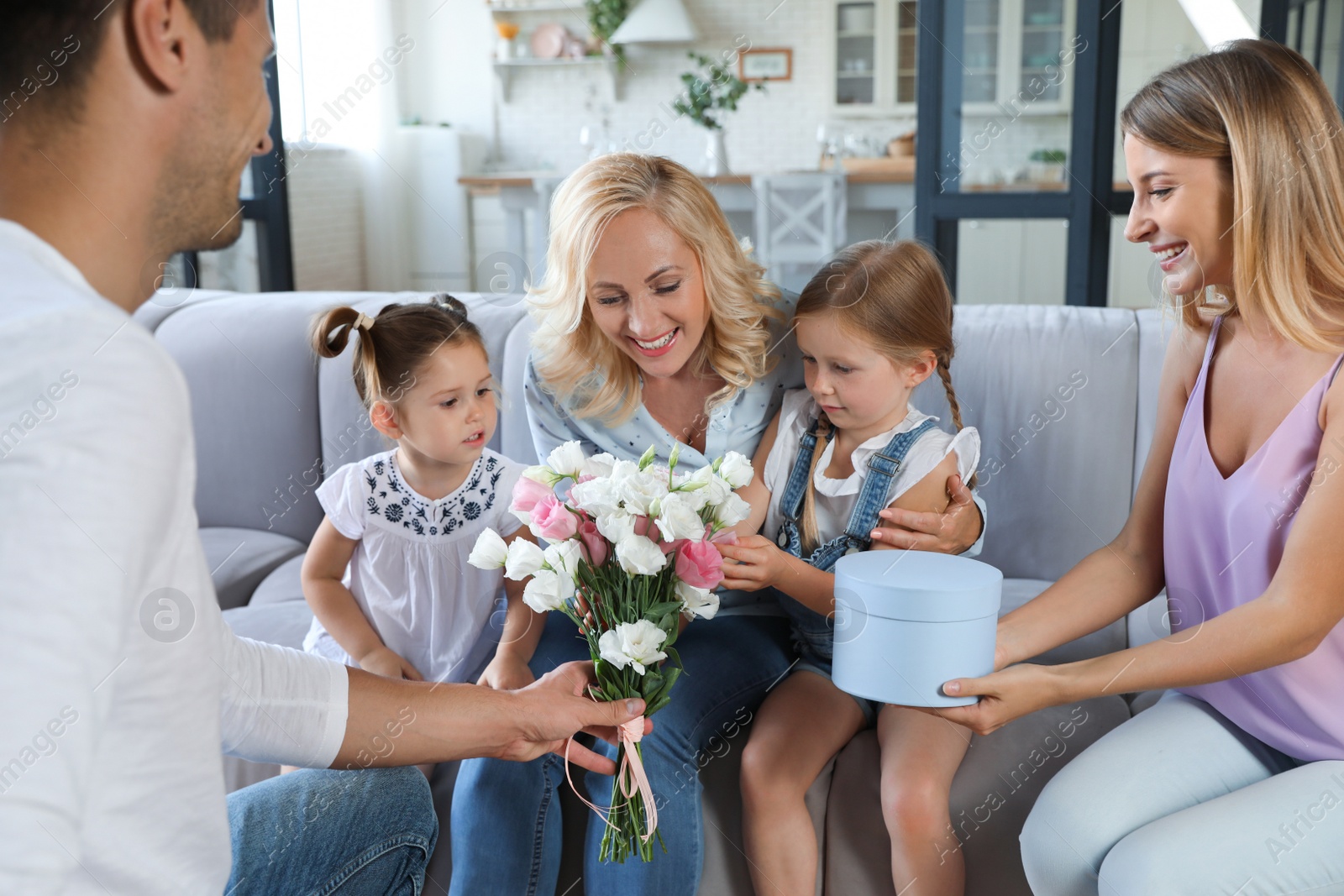 Photo of Happy family with little children congratulating mature woman in living room