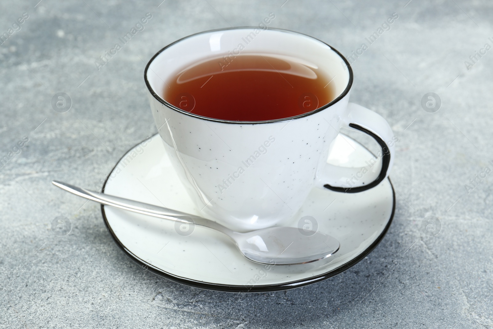 Photo of Aromatic tea in cup and spoon on grey table